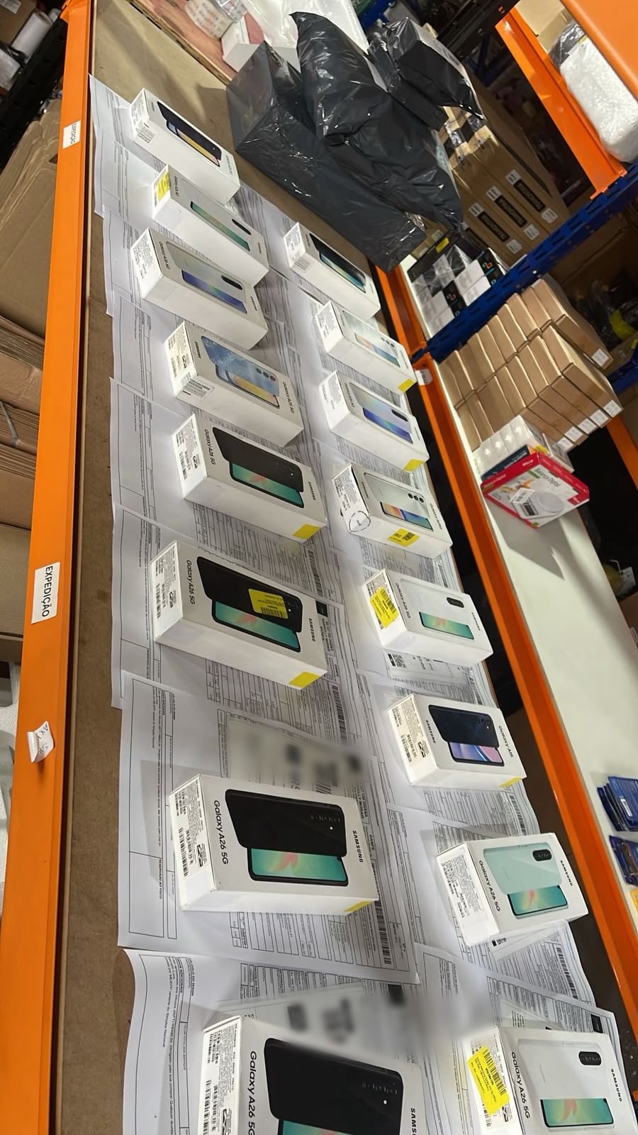 Bancada de expedição com caixas de Galaxy A26 sobre notas fiscais